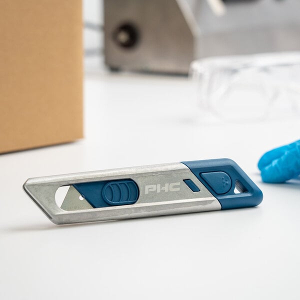 A blue and grey Pacific Handy Cutter Auto-Retract Metti Metal-Detectable Safety Knife on a white surface.