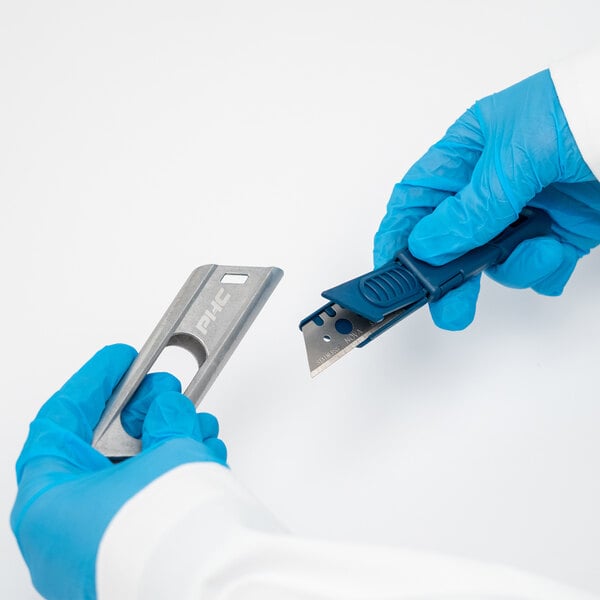 A person in blue gloves using a Pacific Handy Cutter metal-detectable safety knife to cut paper.