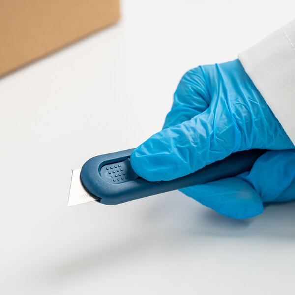 A person in blue gloves using a Pacific Handy Cutter metal-detectable safety knife.