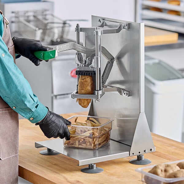 A person in a green apron using a Garde heavy-duty French fry cutter to slice potatoes.