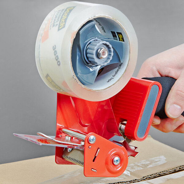 A hand using a 3M Scotch tape dispenser to seal a package.
