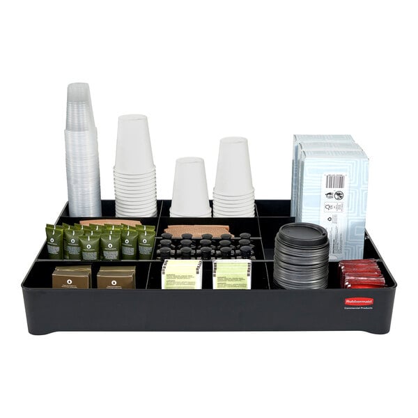 A black Rubbermaid amenity organizer tray holding a variety of coffee items including white cups, lids, and small black containers.