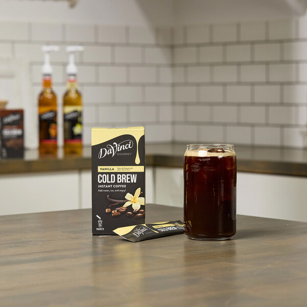 A glass of DaVinci Vanilla Cold Brew next to a box of DaVinci Cold Brew packets.