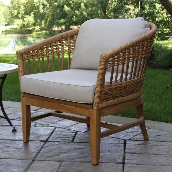 An Outdoor Interiors wicker lounge chair with a cushion on a stone patio.