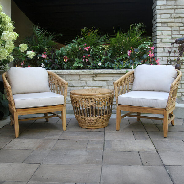 An Outdoor Interiors wicker chair with a cushion next to a wicker table on a patio.