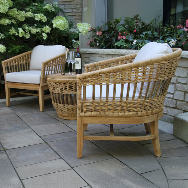 An Outdoor Interiors wicker chair with a white cushion on a patio next to a table set with wine glasses.