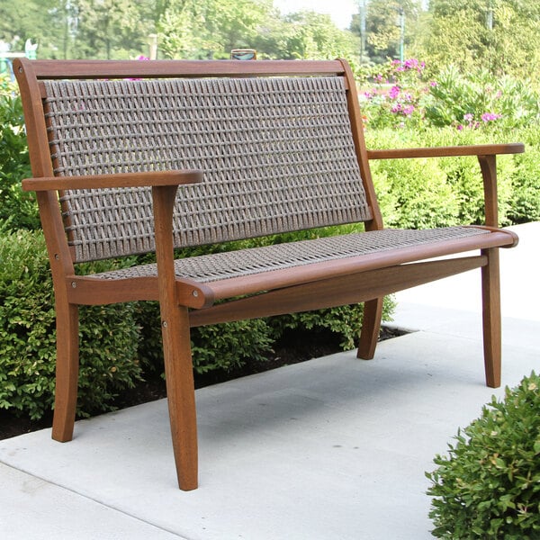 An Outdoor Interiors driftwood gray wooden bench with wicker back on a patio.
