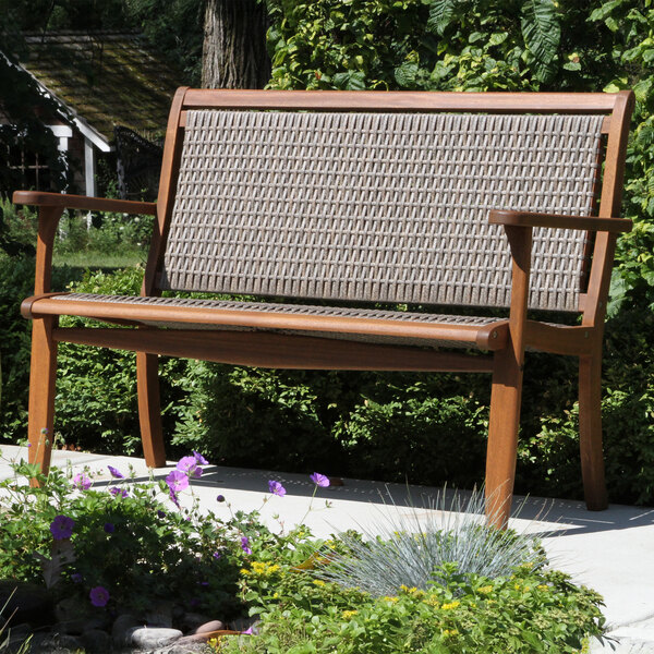 An Outdoor Interiors wicker and eucalyptus bench with a woven seat in a garden.