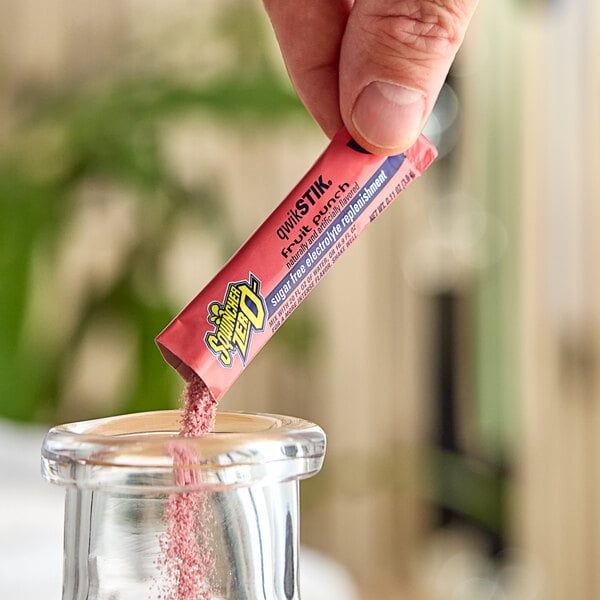 A hand holding a pink Sqwincher QwikStik Zero packet.