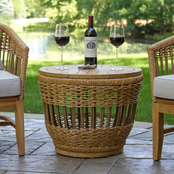 An Outdoor Interiors wicker and teak storage table with wine glasses on top.