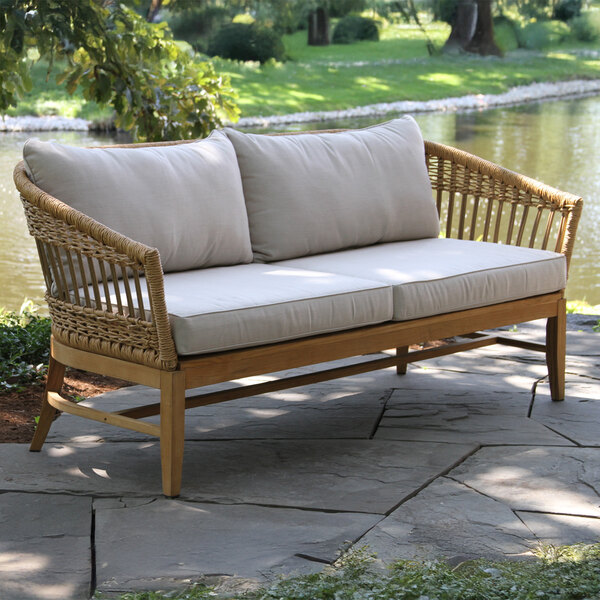 An Outdoor Interiors teak and wicker sofa with white cushions on a stone patio.