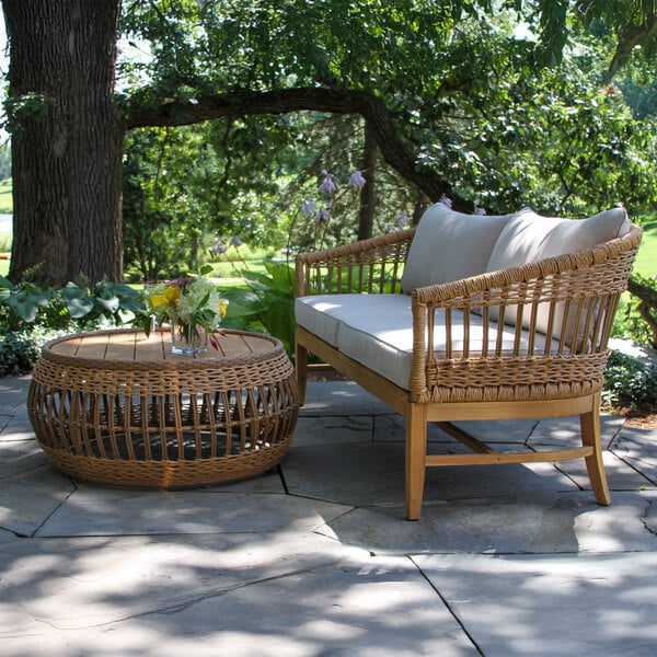An Outdoor Interiors wicker sofa on a stone patio with a wicker table and a vase of flowers.