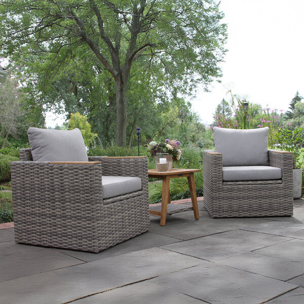 An Outdoor Interiors teak and wicker captain's chair with grey cushion on a patio.