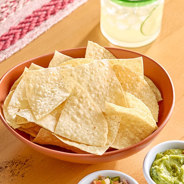 A table with a bowl of Celia's white corn tortilla chips and bowls of salsa and guacamole.