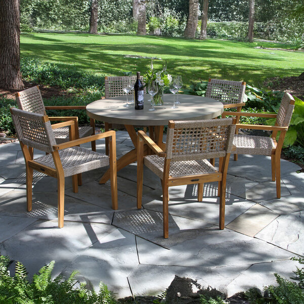 An Outdoor Interiors stackable teak and rope chair on a stone patio with a table set for wine.