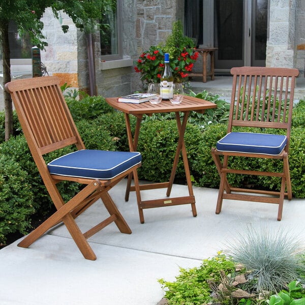 A wooden table with two chairs, one with a blue cushion and red flowers on the table.