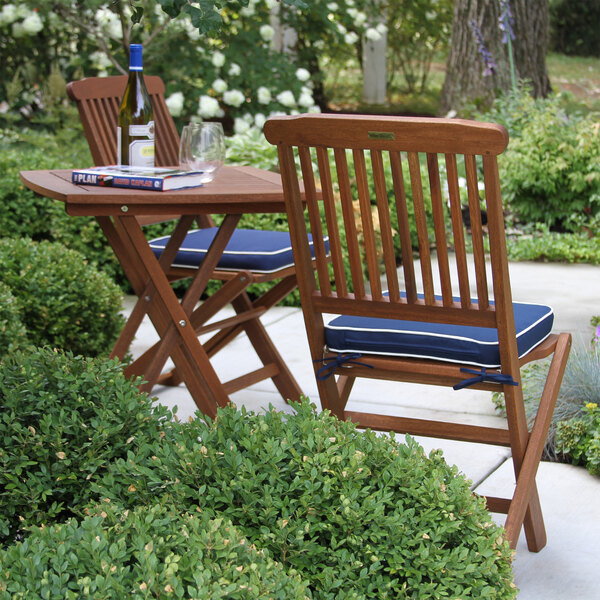 A eucalyptus bistro table and two chairs with blue cushions on an outdoor patio.