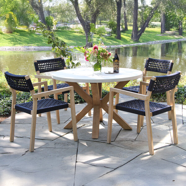 An Outdoor Interiors Blue Rope and Antique Wash Eucalyptus stackable chair on a stone patio next to a table.