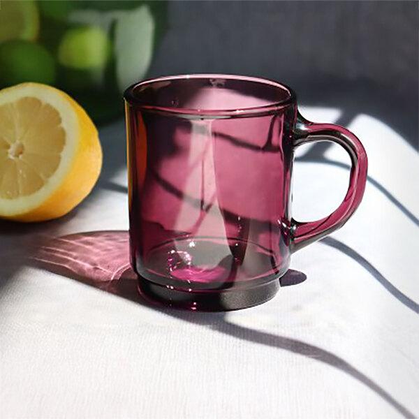 A purple Duralex Versailles glass mug with a handle on a white table next to a lemon.