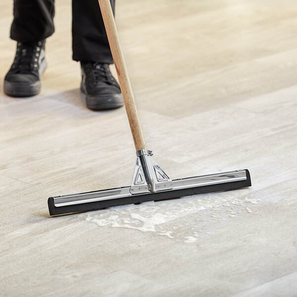 A person using a Lavex black neoprene foam floor squeegee with metal frame and adapters to clean the floor.