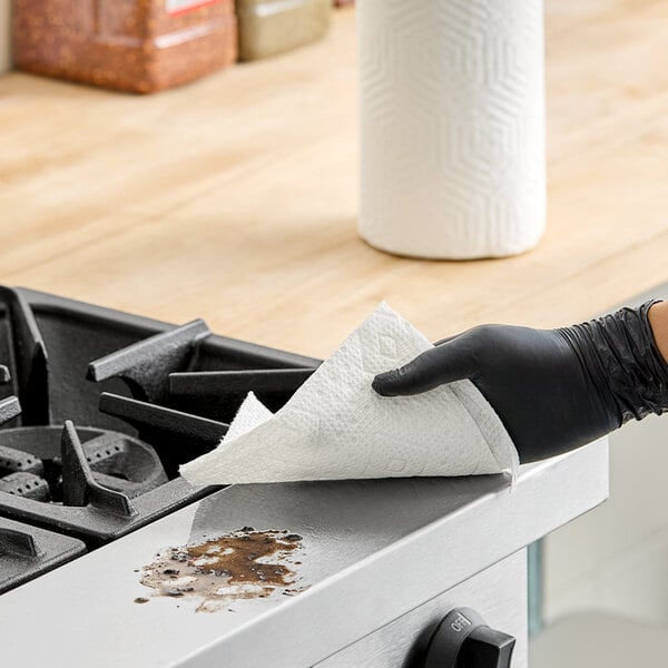 A hand in a black rubber glove using a Bounty Essentials paper towel to clean a stove.