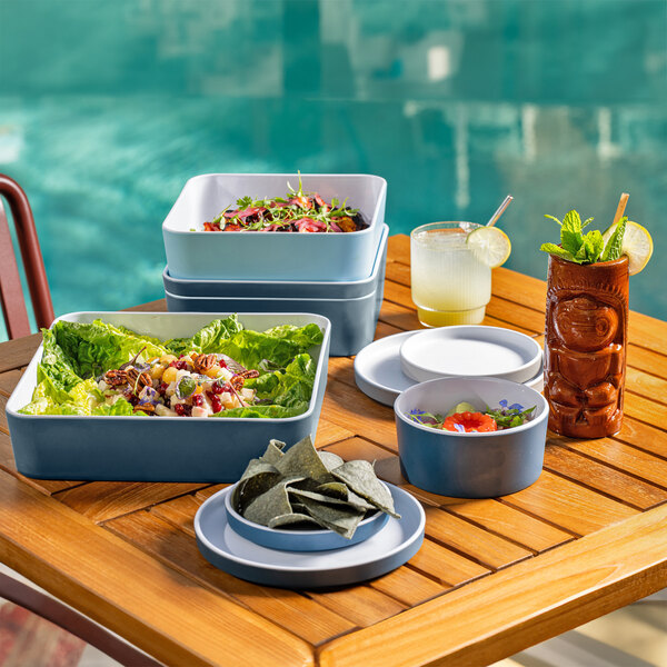 A table with a group of Cal-Mil blue stone square bento boxes filled with food.