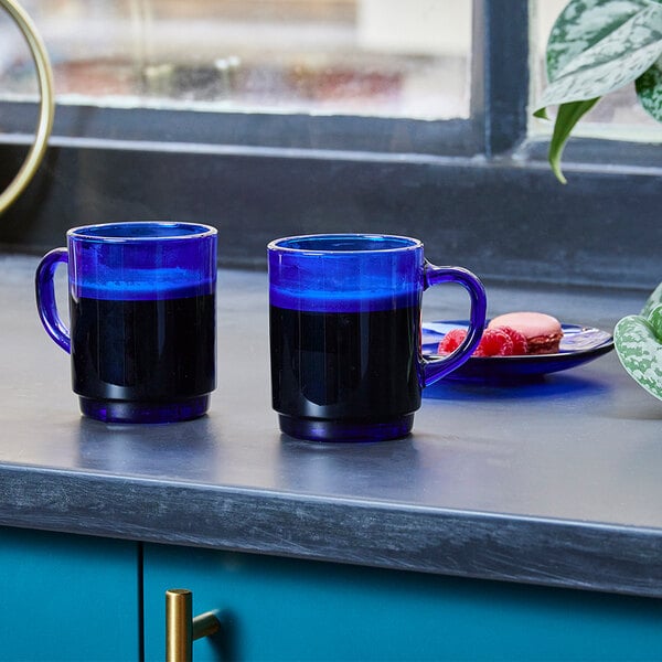 Two Duralex blue glass mugs on a counter.