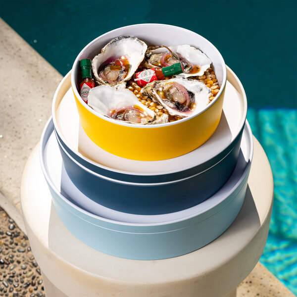 A stack of Cal-Mil round yellow bento boxes filled with oysters and other food items.