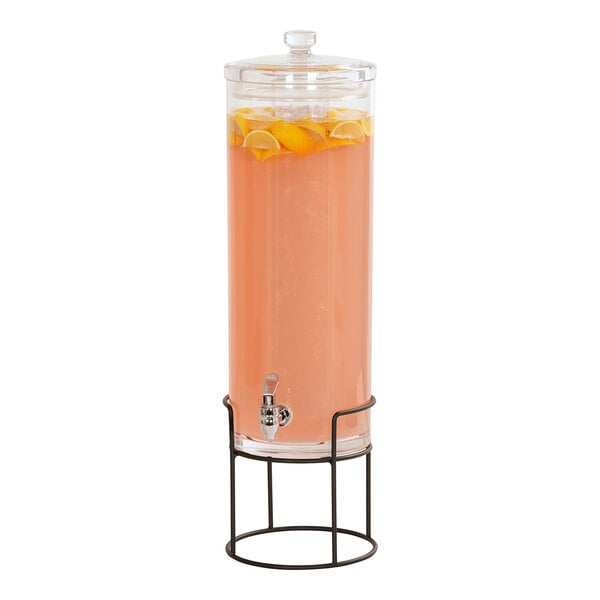 A Cal-Mil glass beverage dispenser with a black wire base filled with orange juice and lemons.