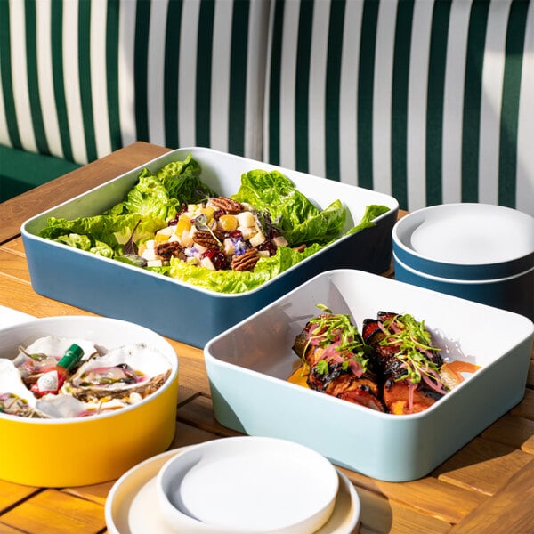 A table with a white bowl of food and a blue square plate of food.
