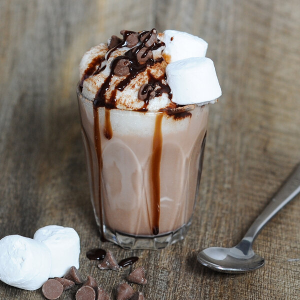 A Duralex glass of chocolate milkshake with marshmallows and a spoon.