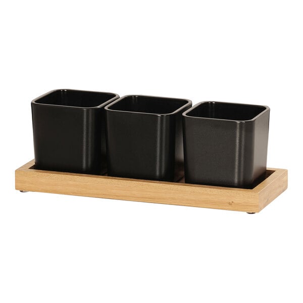 A Cal-Mil oak condiment organizer with three black square containers on a wooden stand.