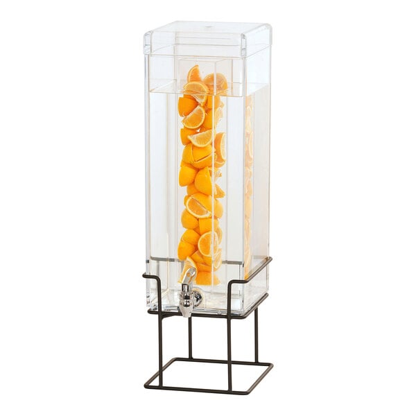 A Cal-Mil square glass beverage dispenser with oranges inside on a black wire base.