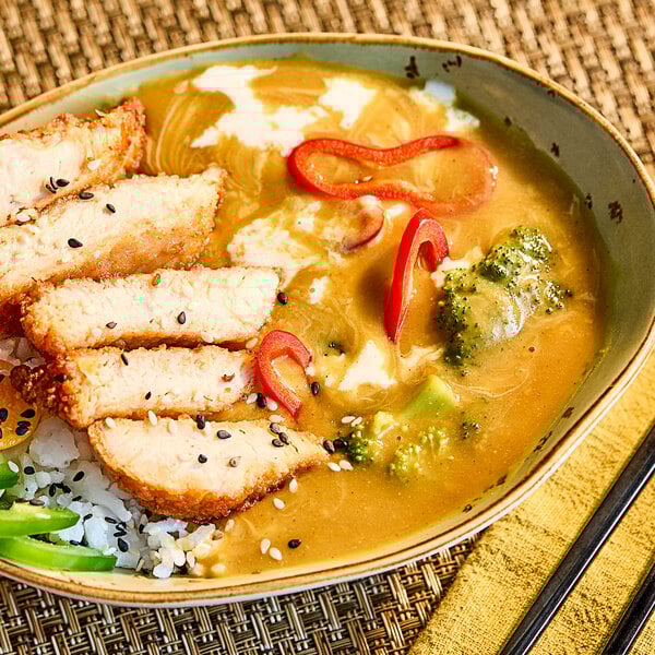 A bowl of Japanese curry with sliced breaded chicken, rice, broccoli, and red pepper, served with S&B Medium Hot Golden Curry Sauce.
