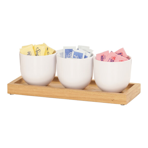 A Cal-Mil oak condiment organizer with three white cups holding different colored packets.