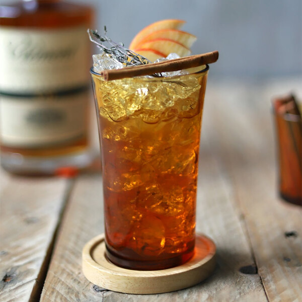 A Duralex amber glass filled with brown liquid and ice with an orange slice and cinnamon stick.