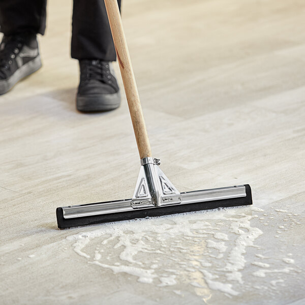A person using a Lavex black neoprene floor squeegee to clean the floor.