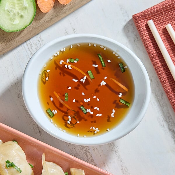 A bowl of Viet Huong fish sauce next to a bowl of soup with chopsticks and vegetables.