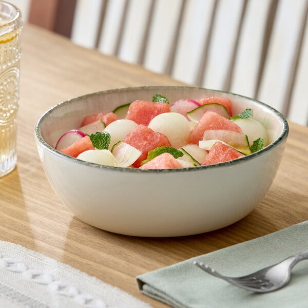 A round gray porcelain bowl filled with a fresh fruit and vegetable salad, placed on a wooden table.