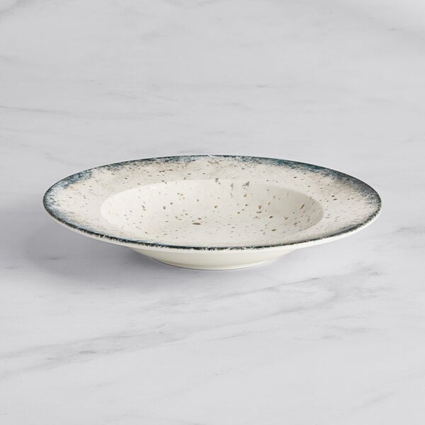 An Acopa Architect white porcelain bowl with blue specks on a marble surface.