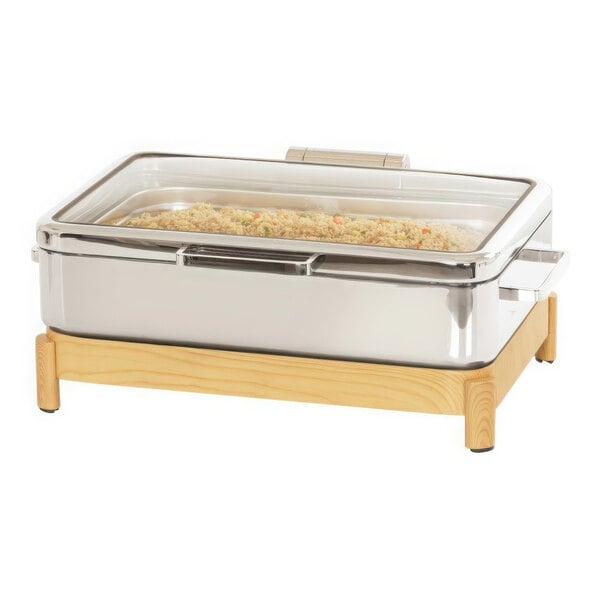 A stainless steel chafing dish with food inside on a wooden stand.