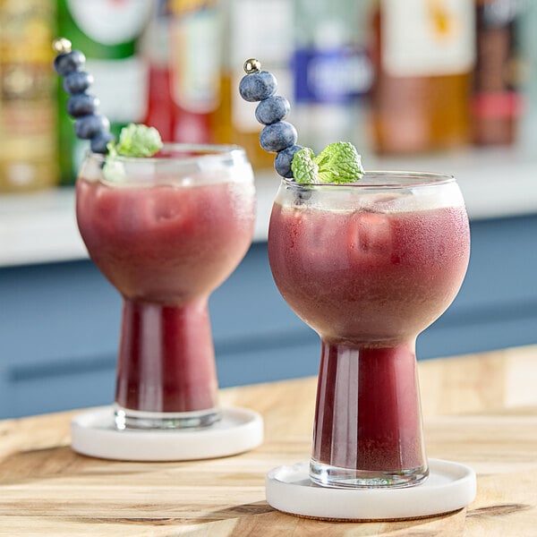 Two glasses of red acai berry cocktails garnished with blueberries and mint leaves on a wooden bar.