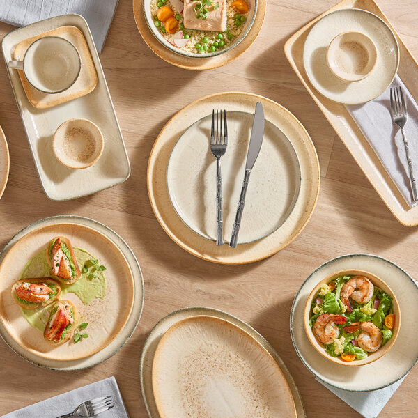 A beige 6-inch round porcelain saucer displayed with other matching dinnerware on a wooden table.