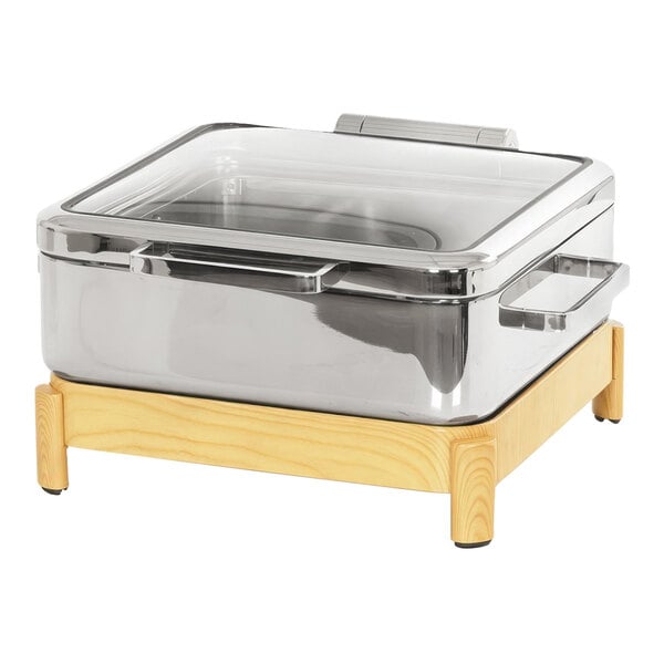 A stainless steel chafing dish with a wooden and silver stand and a clear glass lid.