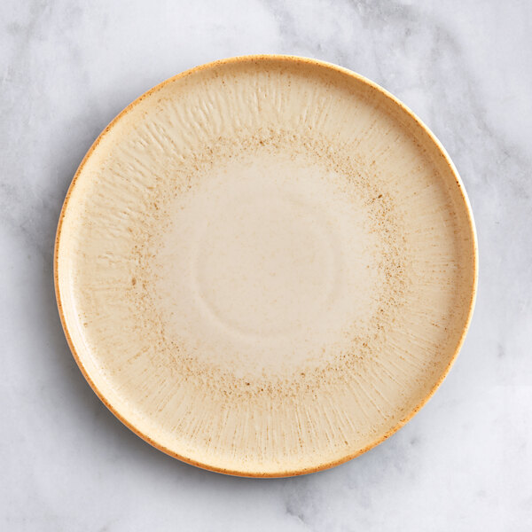 An Acopa Cape beige porcelain plate with a brown rim on a white surface with brown specks.