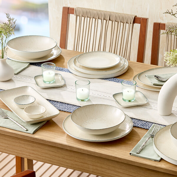 A set of round gray porcelain coupe plates arranged on a dining table with other tableware and decor.
