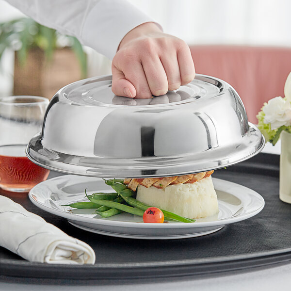 A stainless steel plate cover with a mirror finish being lifted off a plated meal.