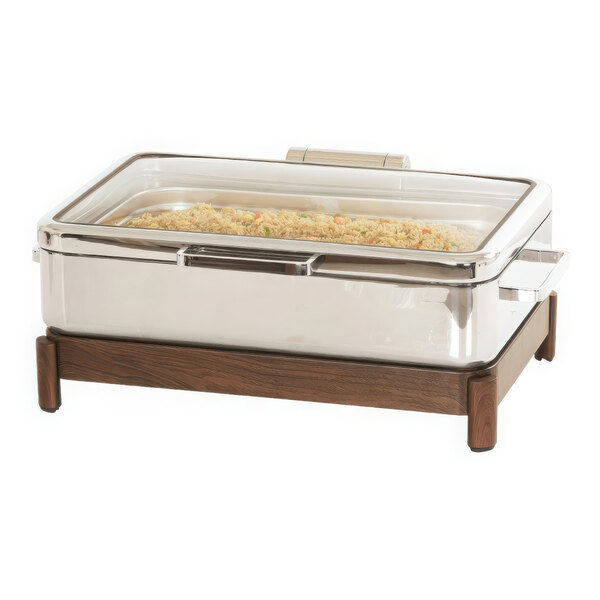 A stainless steel chafer with food inside on a table with a wood and stainless steel stand.