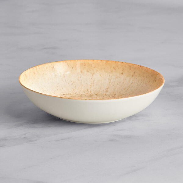 An Acopa Cape beige porcelain deep coupe plate with brown spots on the rim.