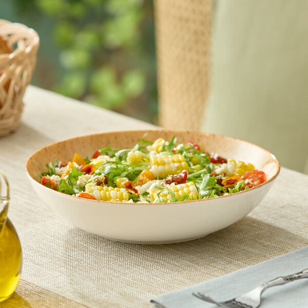 A round beige porcelain deep coupe plate filled with salad, placed on a table.